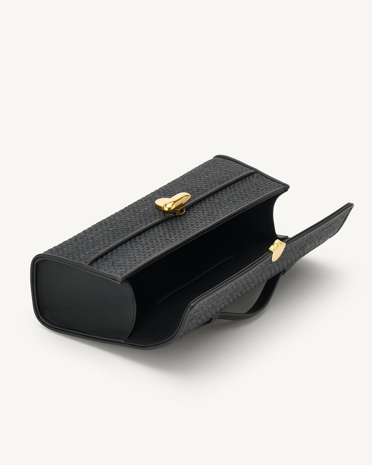 interior view of a black raffia bag with leather trim with a gold clasp on a white background