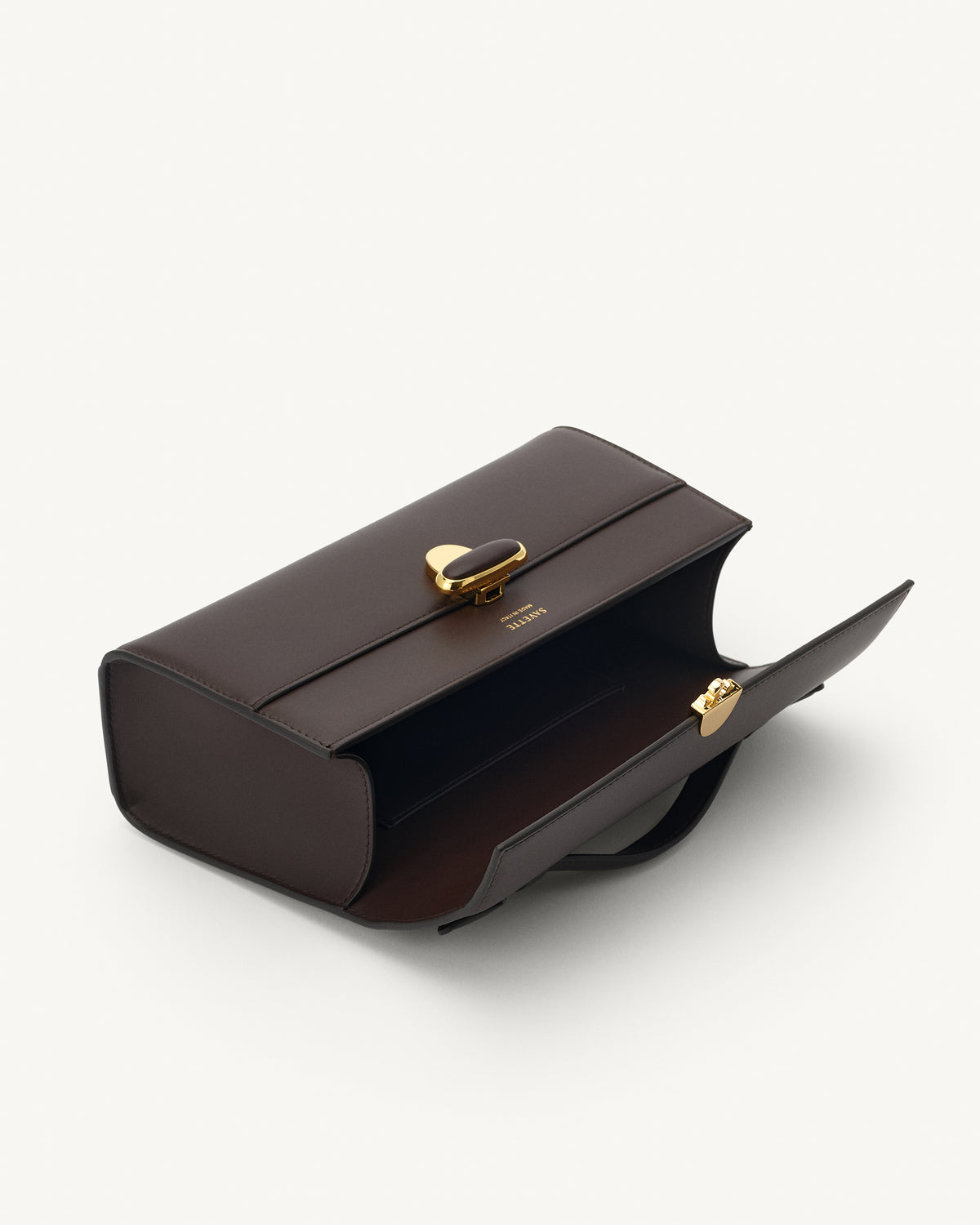 interior view of a coffee brown leather top handle bag with a coffee brown leather covered gold clasp on a white background