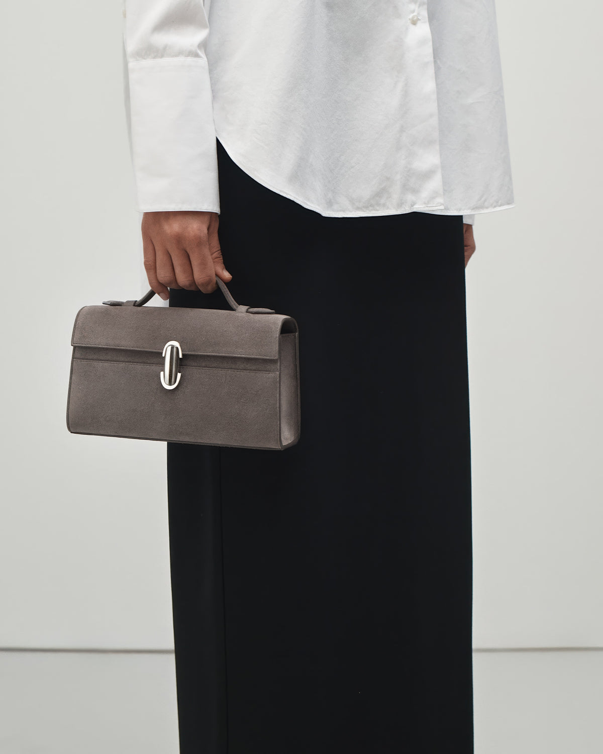 interior view of a smoke grey suede top handle bag with a silver clasp on a white background