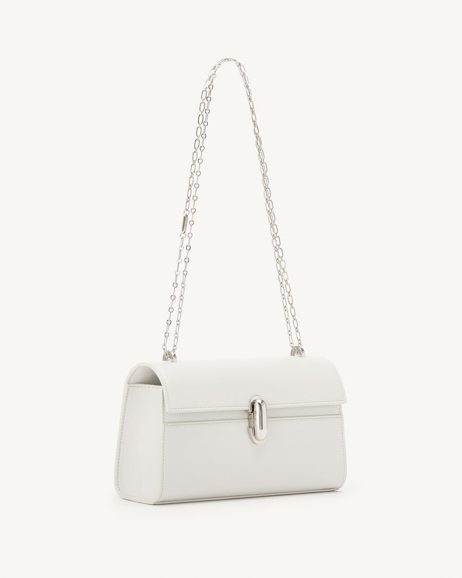 side view of an ivory leather bag with silver clasp and silver chain on a white background
