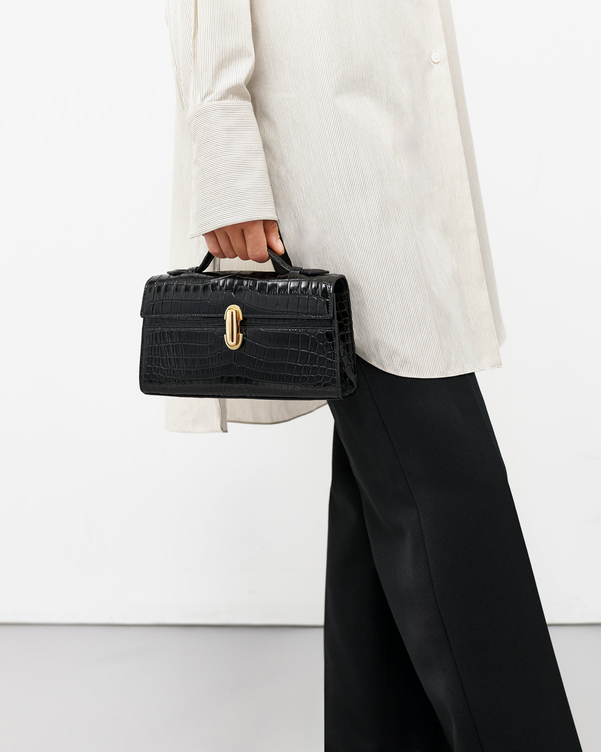 on model image of a black crocodile bag with a gold clasp on a white background