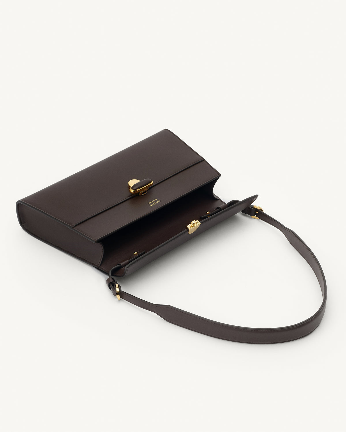 interior view of a coffee brown leather shoulder bag with a leather covered gold clasp on a white background 