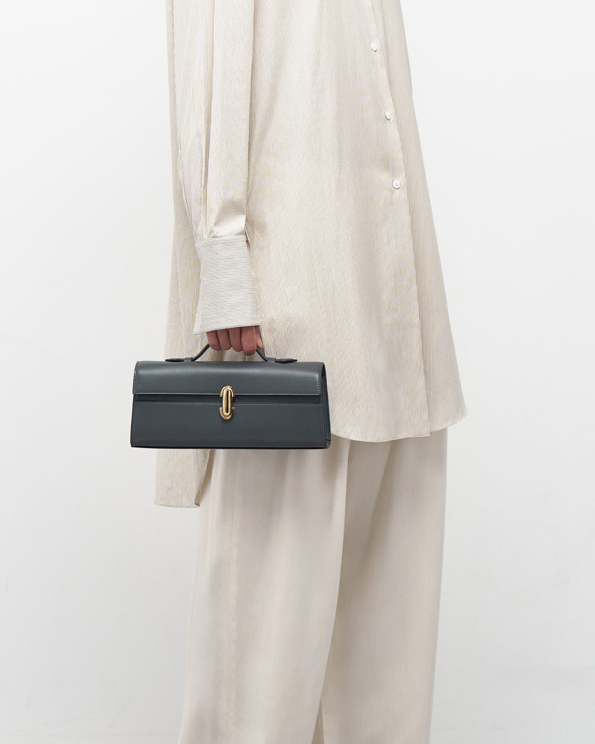 on model view of a storm blue leather bag with a gold clasp on a white background