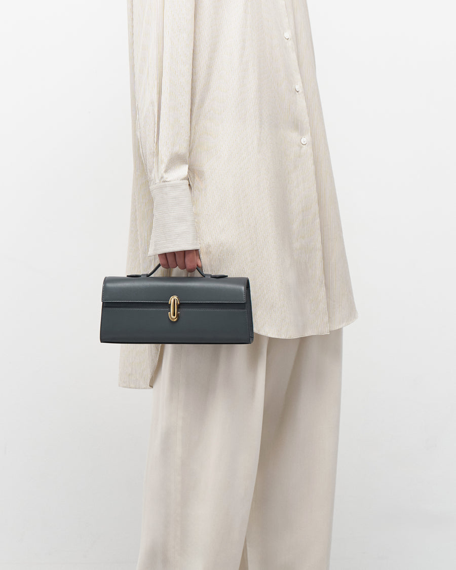 on model view of a storm blue leather bag with a gold clasp on a white background