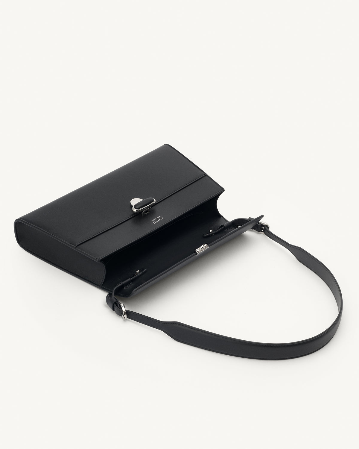 interior view of a black leather shoulder bag with a black leather covered silver clasp on a white background