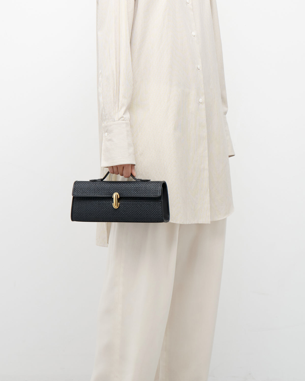 on model view of a black raffia bag with a gold clasp on a white background