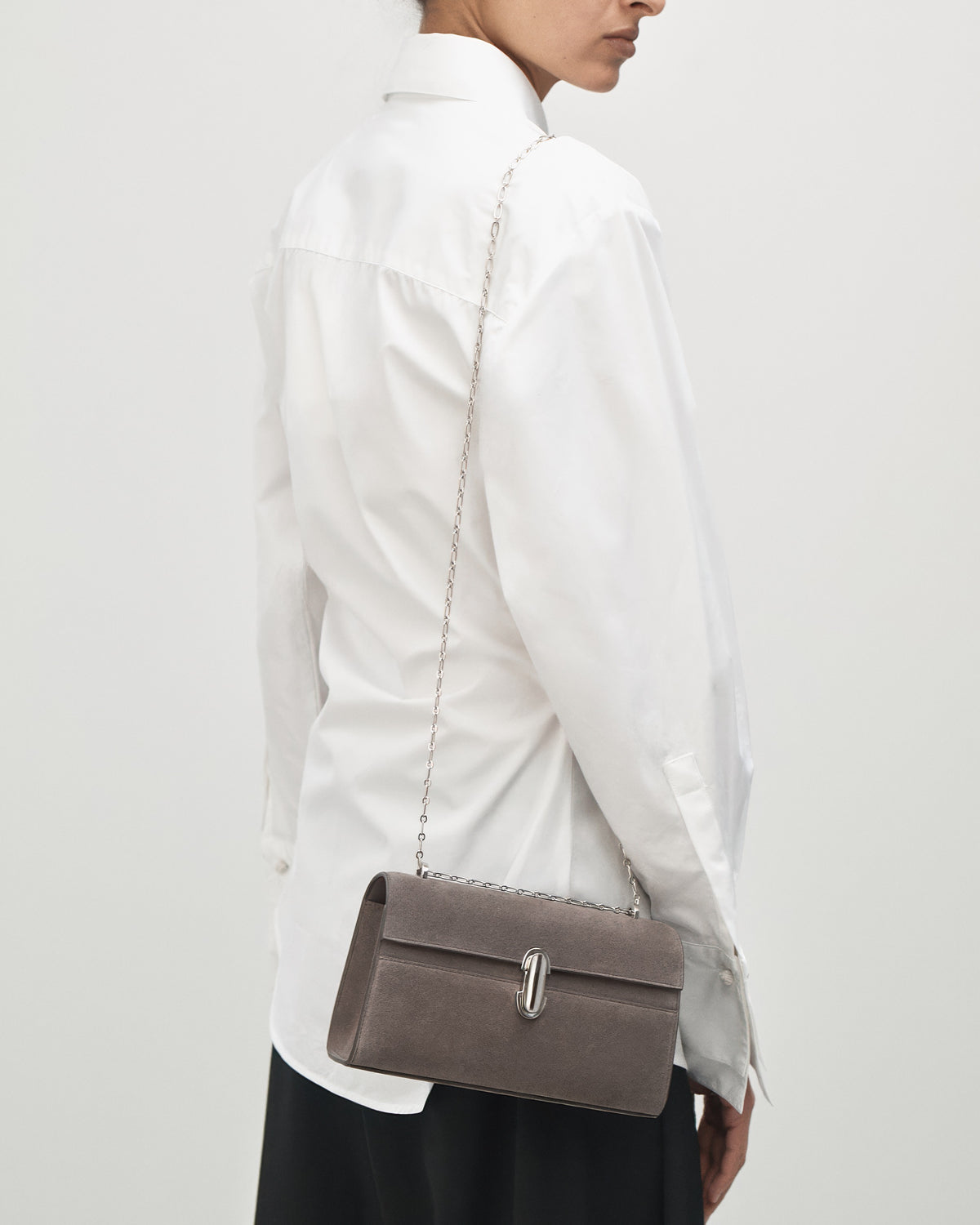 on-model view of a smoke grey suede bag with a silver chain and silver clasp on a white background 
