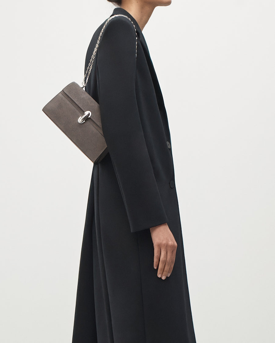 on-model view of a smoke grey suede bag with a silver chain and silver clasp on a white background 