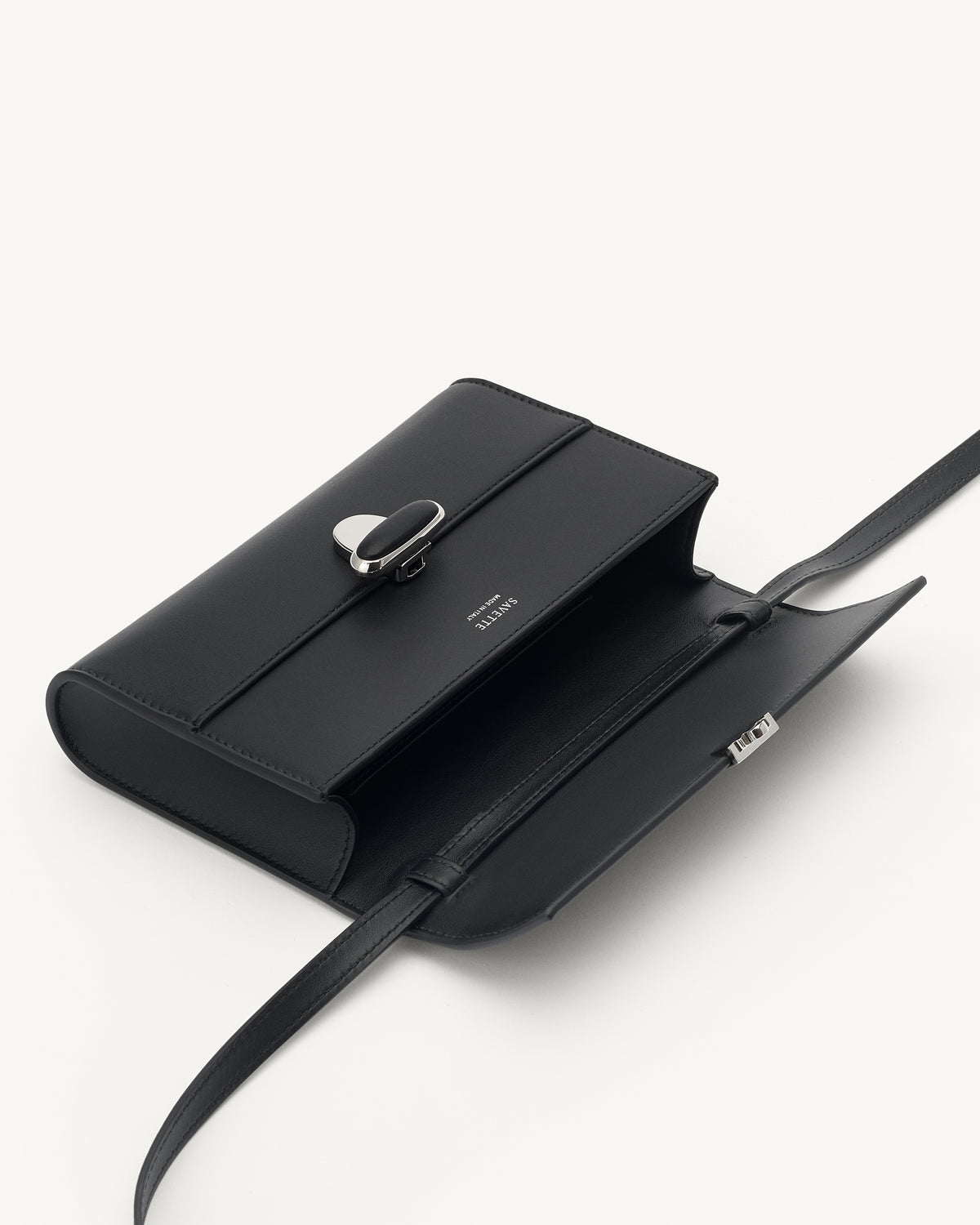 interior view of a black leather handbag with a black leather covered silver clasp on a white background 