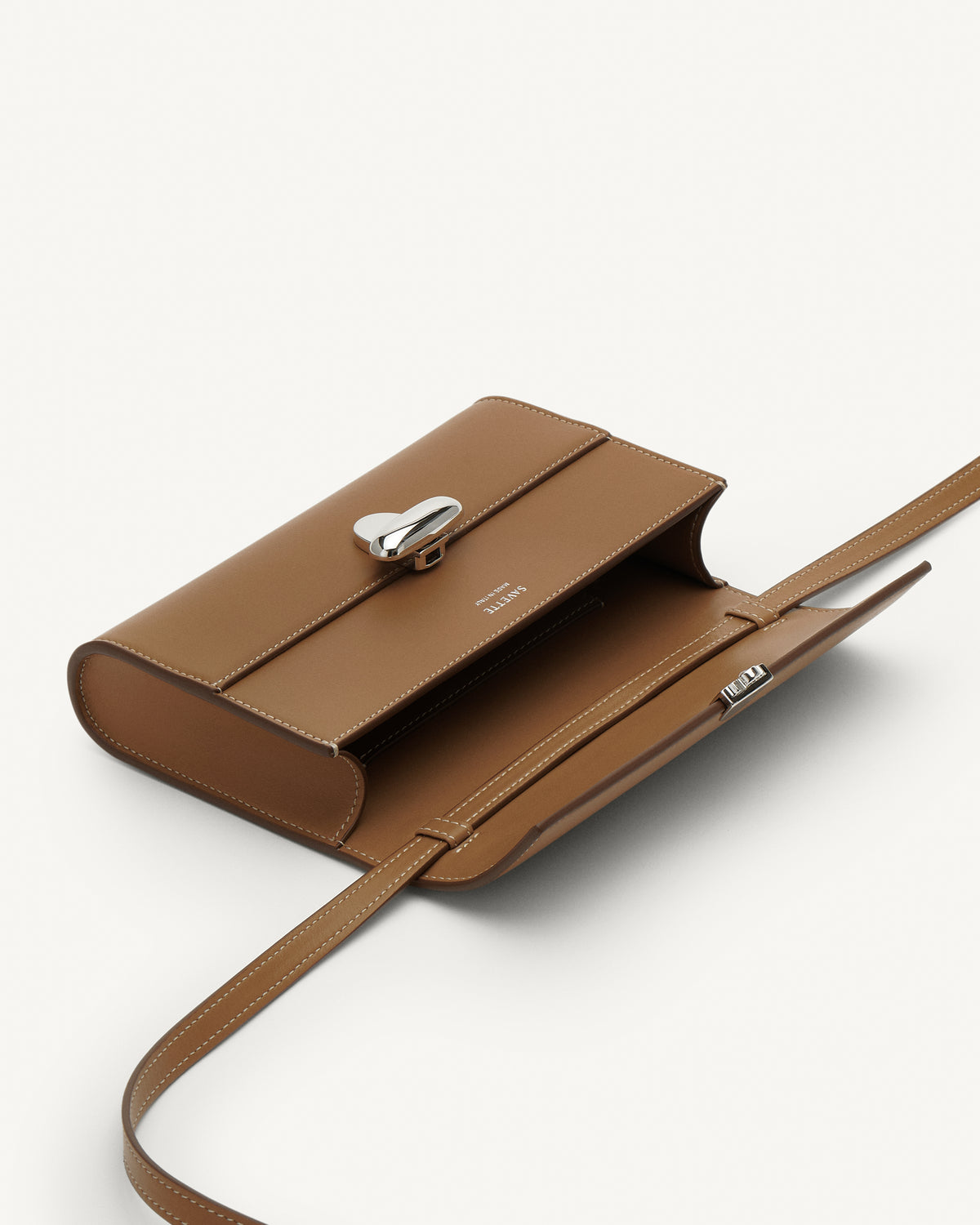 Inside view of saddle leather handbag with silver hardware and a crossbody strap on a white background