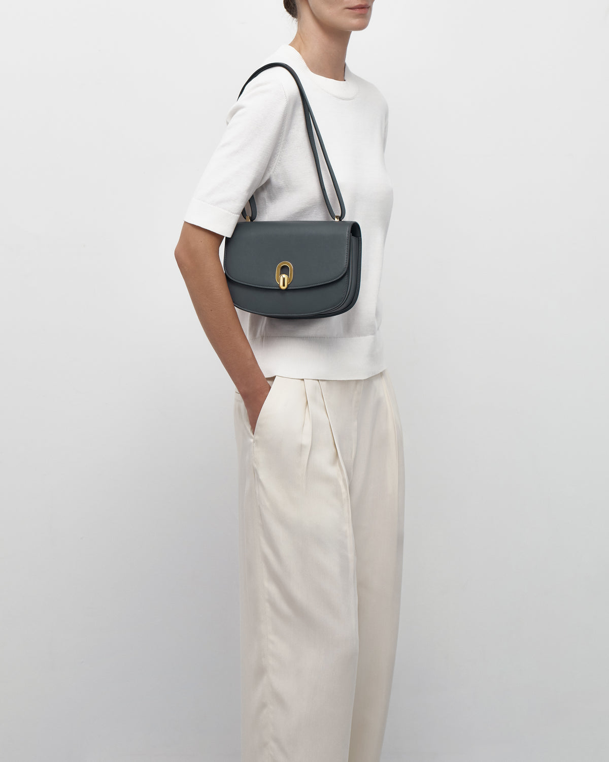 on model view of a storm blue leather bag with a gold clasp on a white background