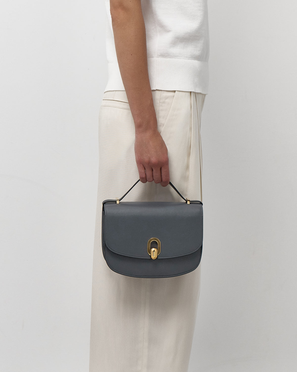 on model view of a storm blue leather bag with a gold clasp on a white background
