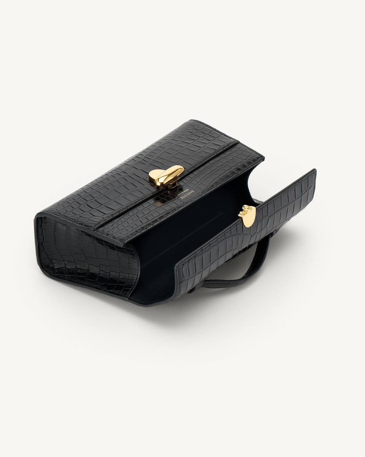 interior view of a black crocodile bag with a gold clasp on a white background