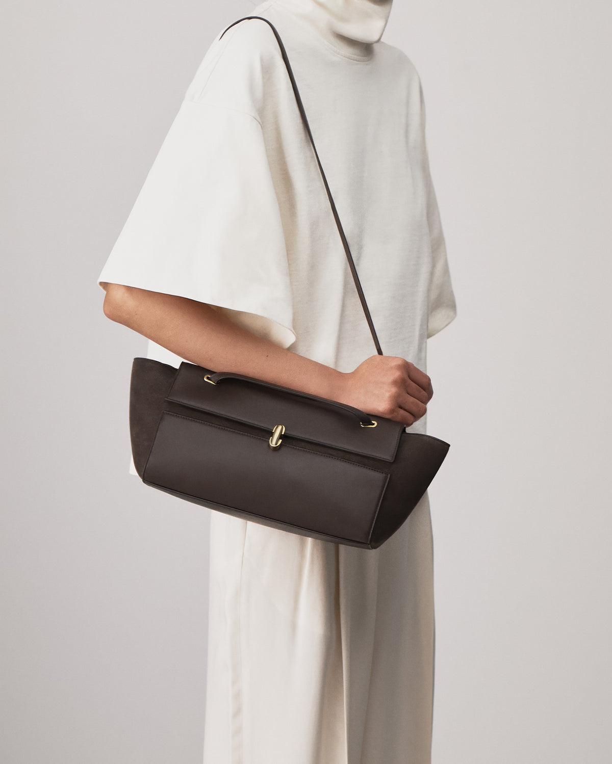 on model view of a coffee brown smooth and suede leather shoulder bag with a gold clasp on a white background