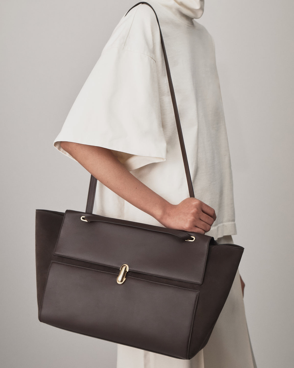on model view of a coffee brown smooth and suede leather tote bag with a gold clasp on a white background 