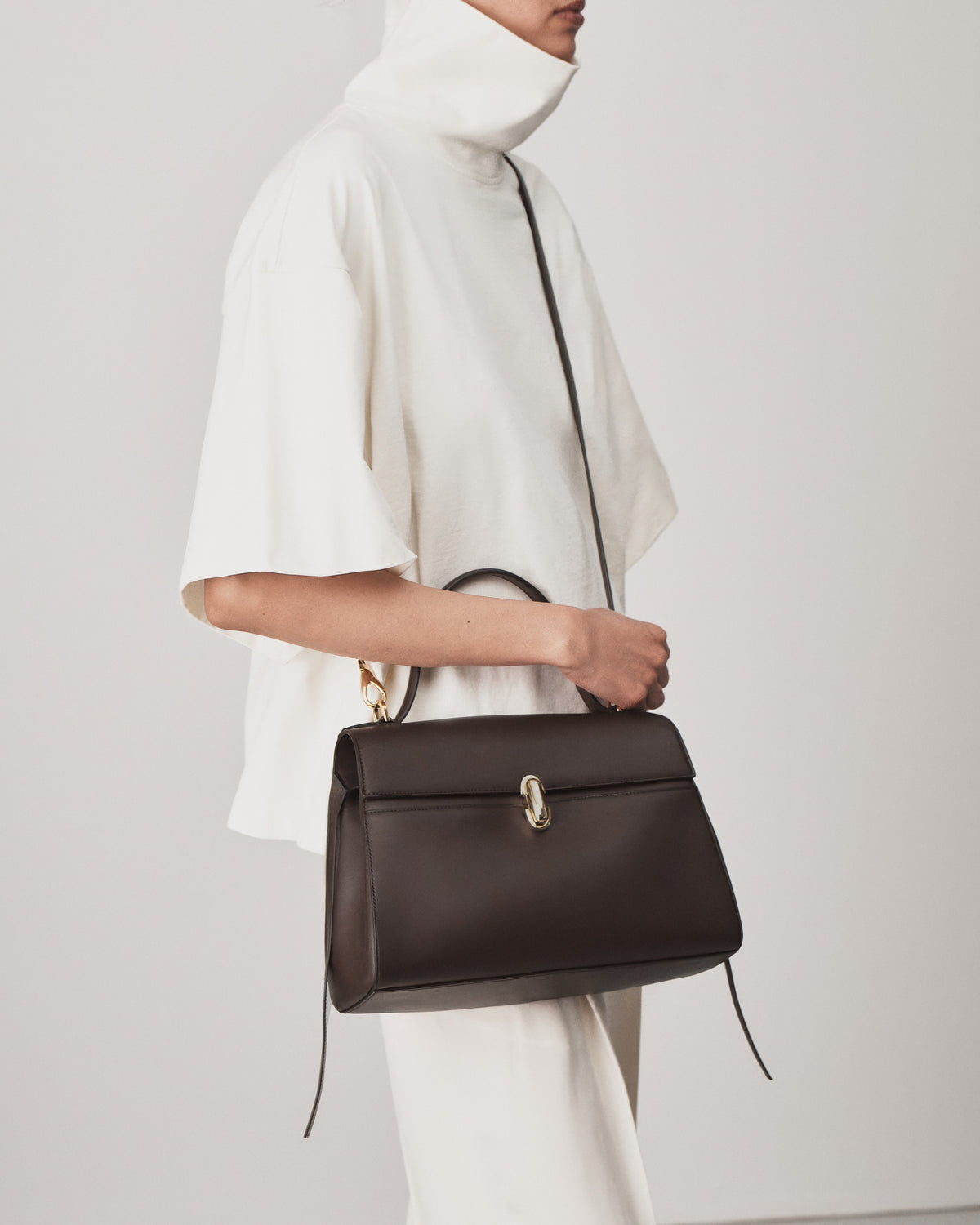 on model view of a coffee brown leather bag with a gold clasp on a white background