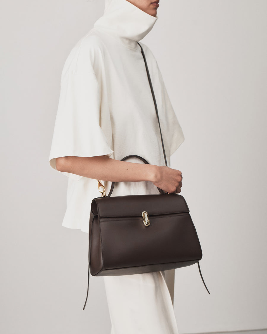 on model view of a coffee brown leather bag with a gold clasp on a white background