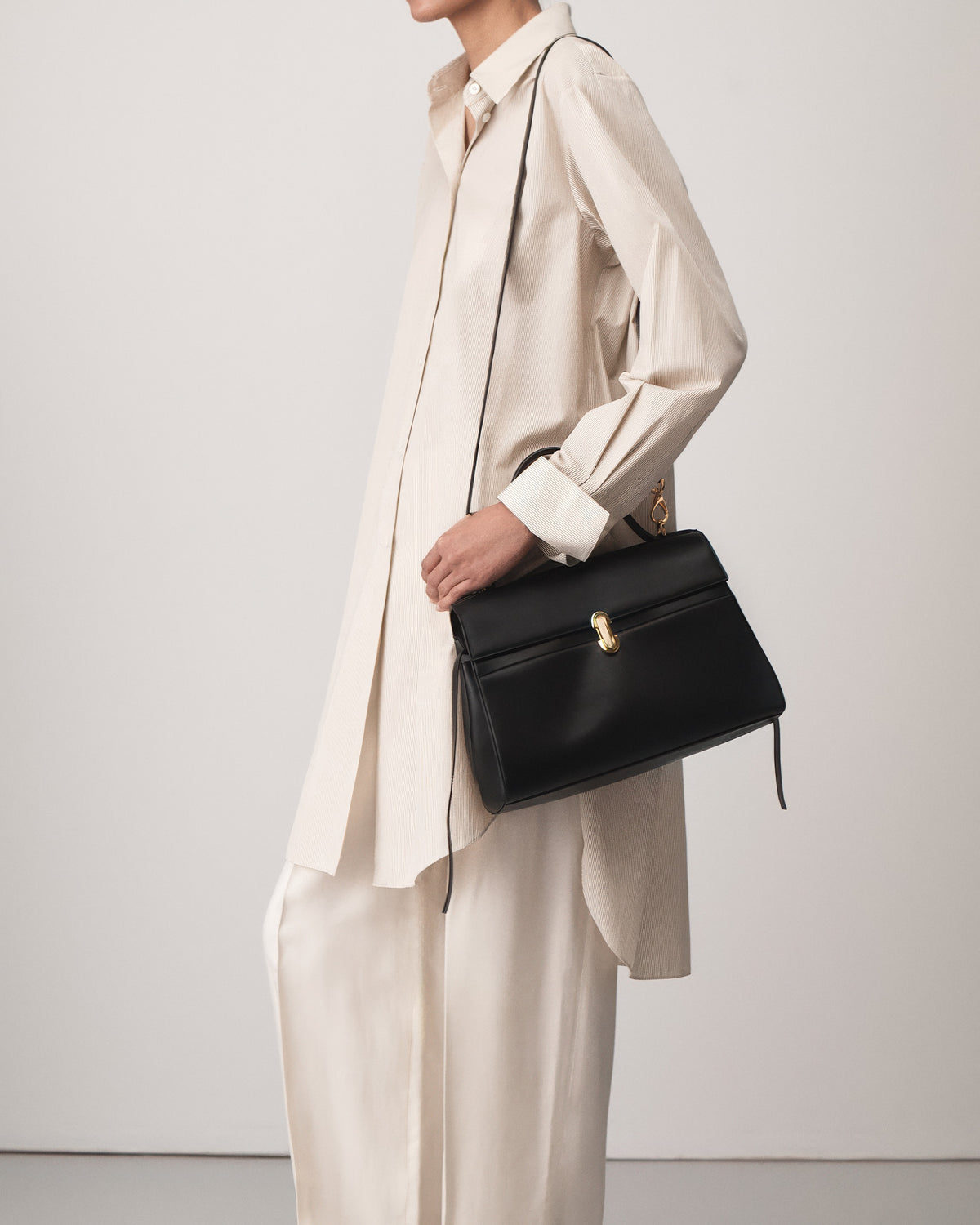 on-model view of a black leather handbag with gold clasp on a white background 