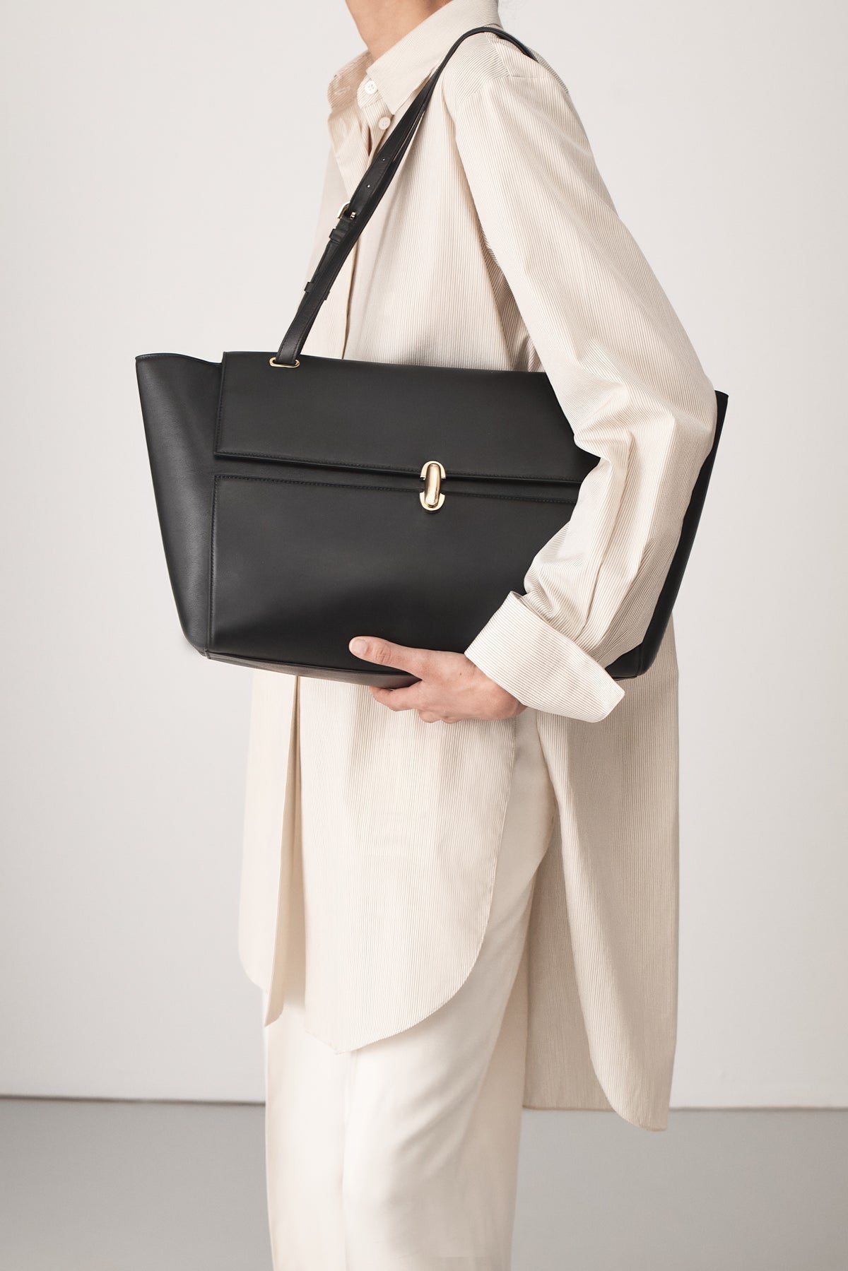 on-model view of a black leather tote bag with a gold clasp on a white background 