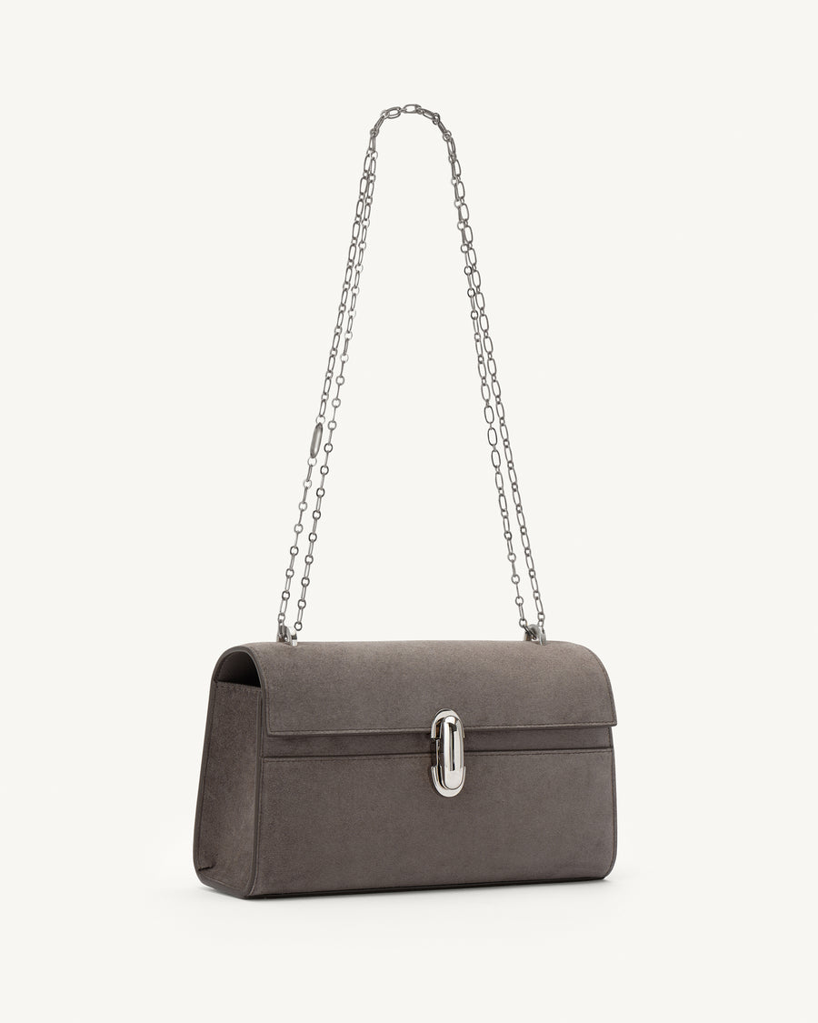 side view of a smoke grey suede bag with a silver chain and silver clasp on a white background 