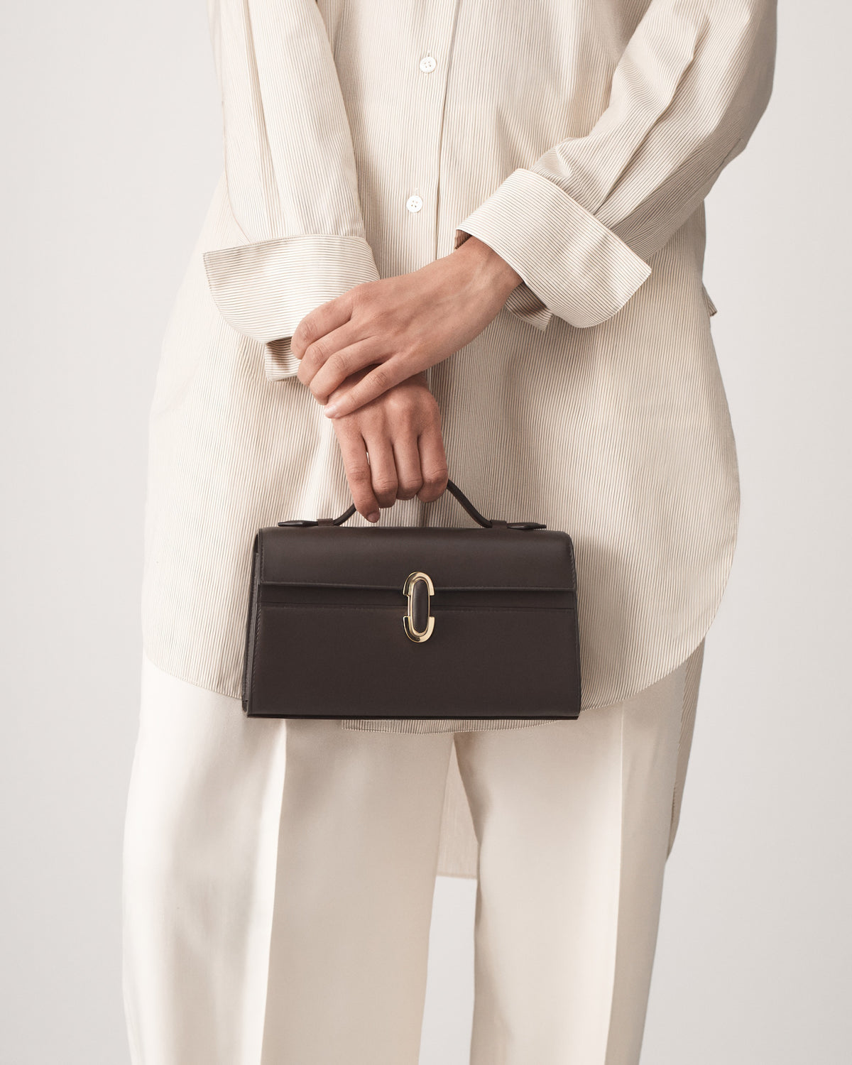on model view of a coffee brown leather top handle bag with a coffee brown leather covered gold clasp on a white background