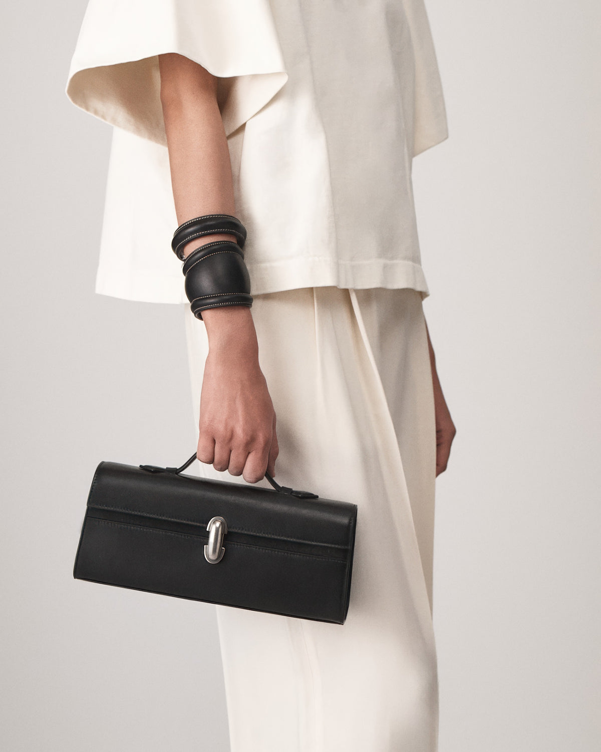 on-model view of vintage black leather top handle bag with matte silver clasp on a white background 