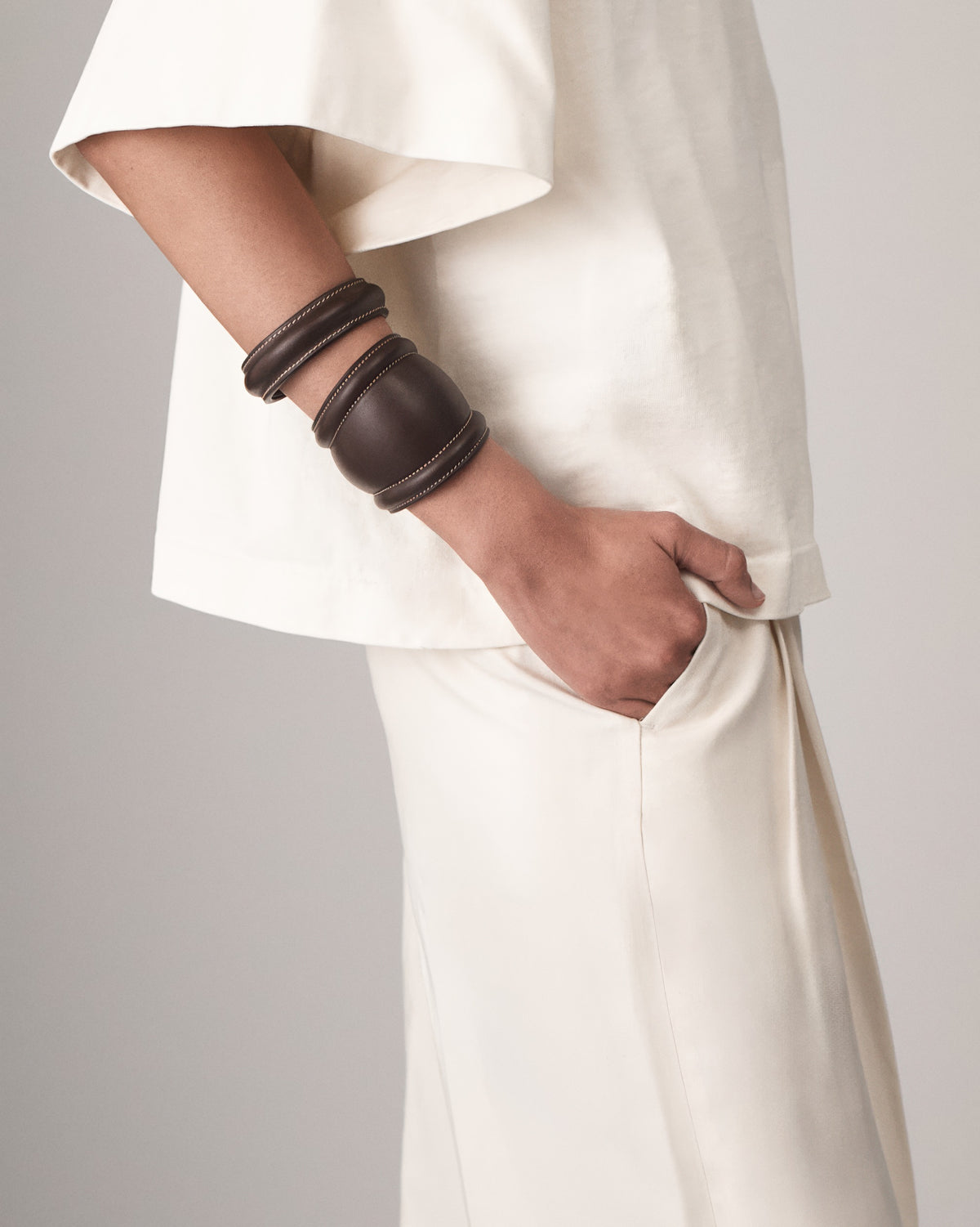 on model view of a coffee brown leather bangle with white stitching on a white background
