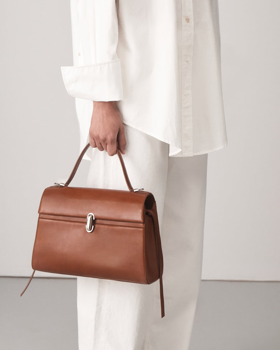 on-model view of a cognac brown leather bag with a silver clasp on a white background 