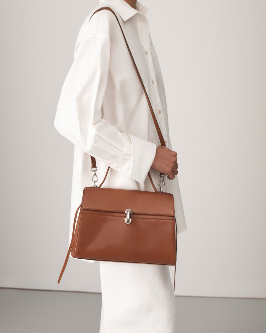 on-model view of a cognac brown leather bag with a silver clasp on a white background 