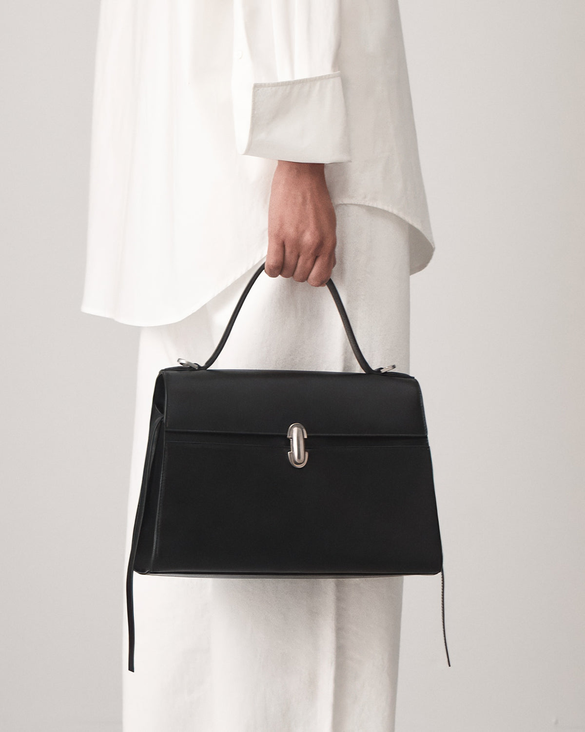 on model view of a black leather handbag with a silver clasp on a white background