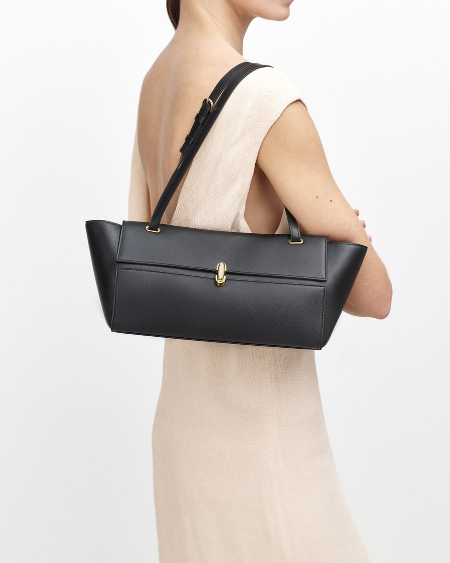 on-model view of a black leather bag with a gold clasp on a white background 