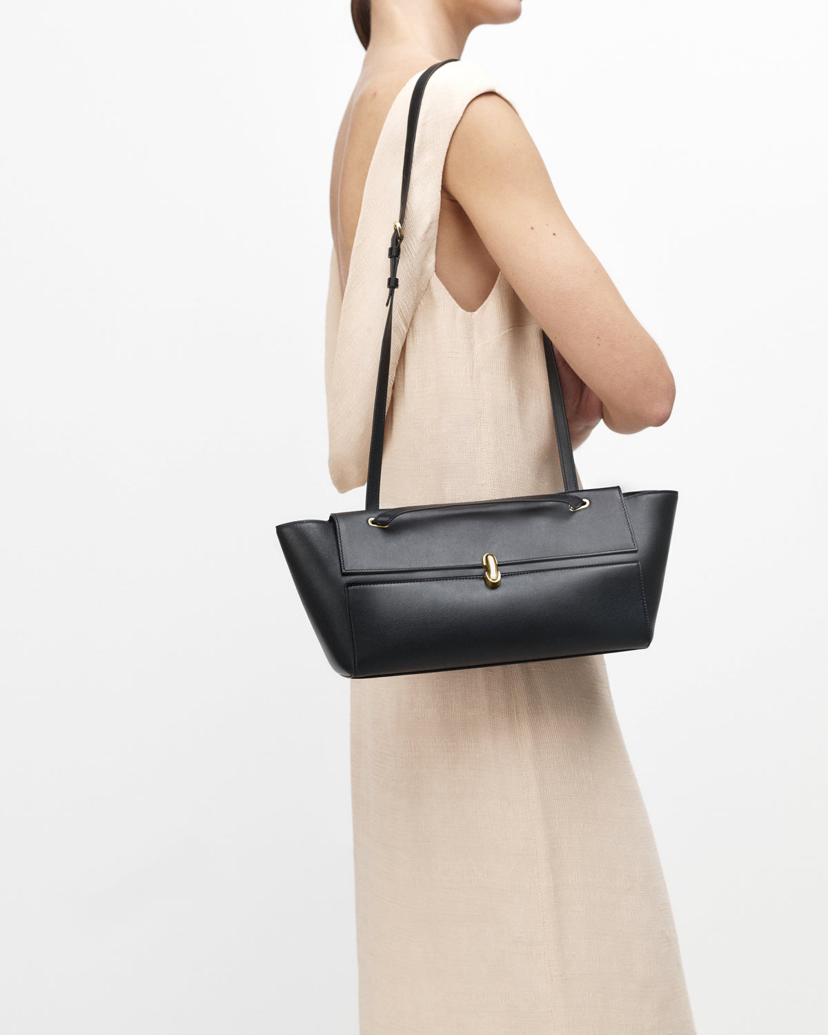 on-model view of a black leather bag with a gold clasp on a white background 