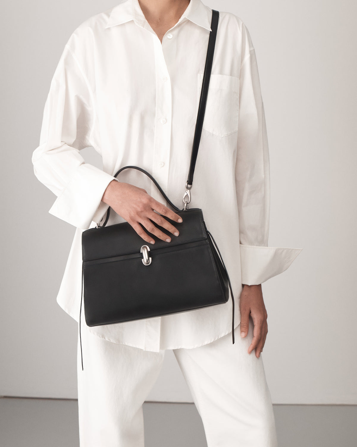 on model view of a black leather handbag with a silver clasp on a white background