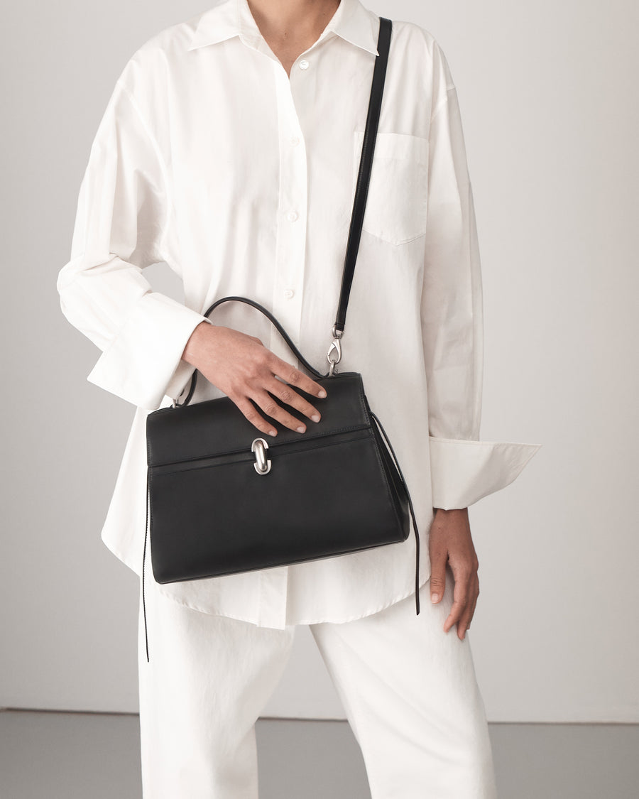 on model view of a black leather handbag with a silver clasp on a white background