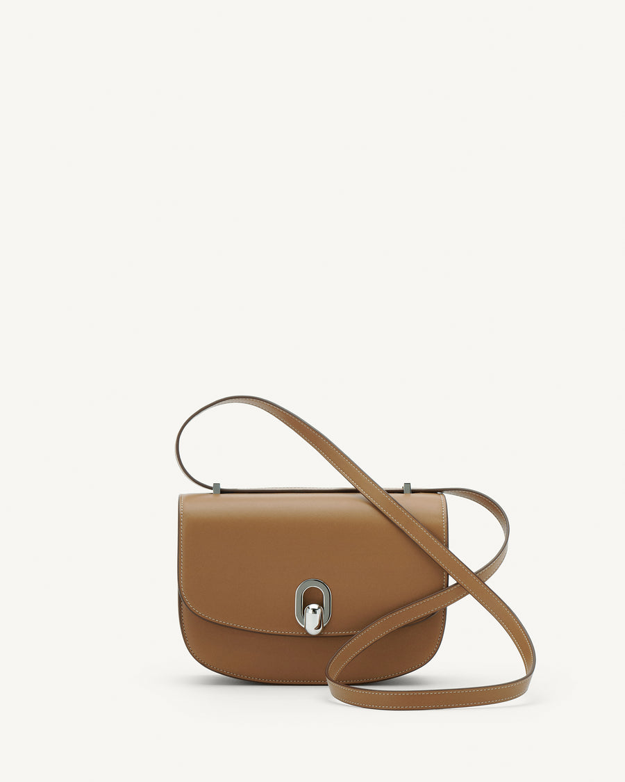 Front view of saddle leather handbag with silver hardware and a crossbody strap on a white background
