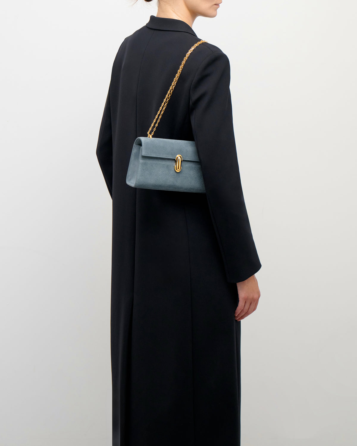 on model view of a denim blue suede bag with gold clasp and chain on a white background