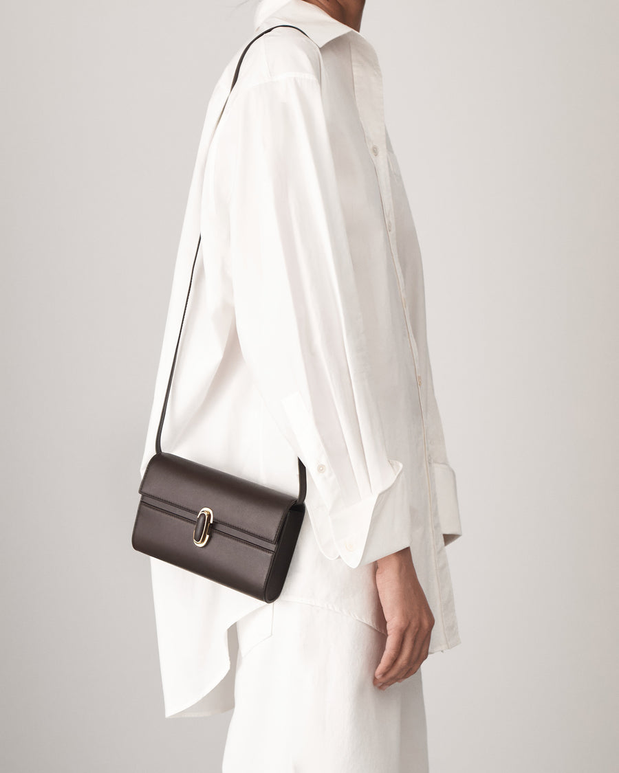 on model view of a coffee brown leather bag with a coffee brown leather covered gold clasp on a white background