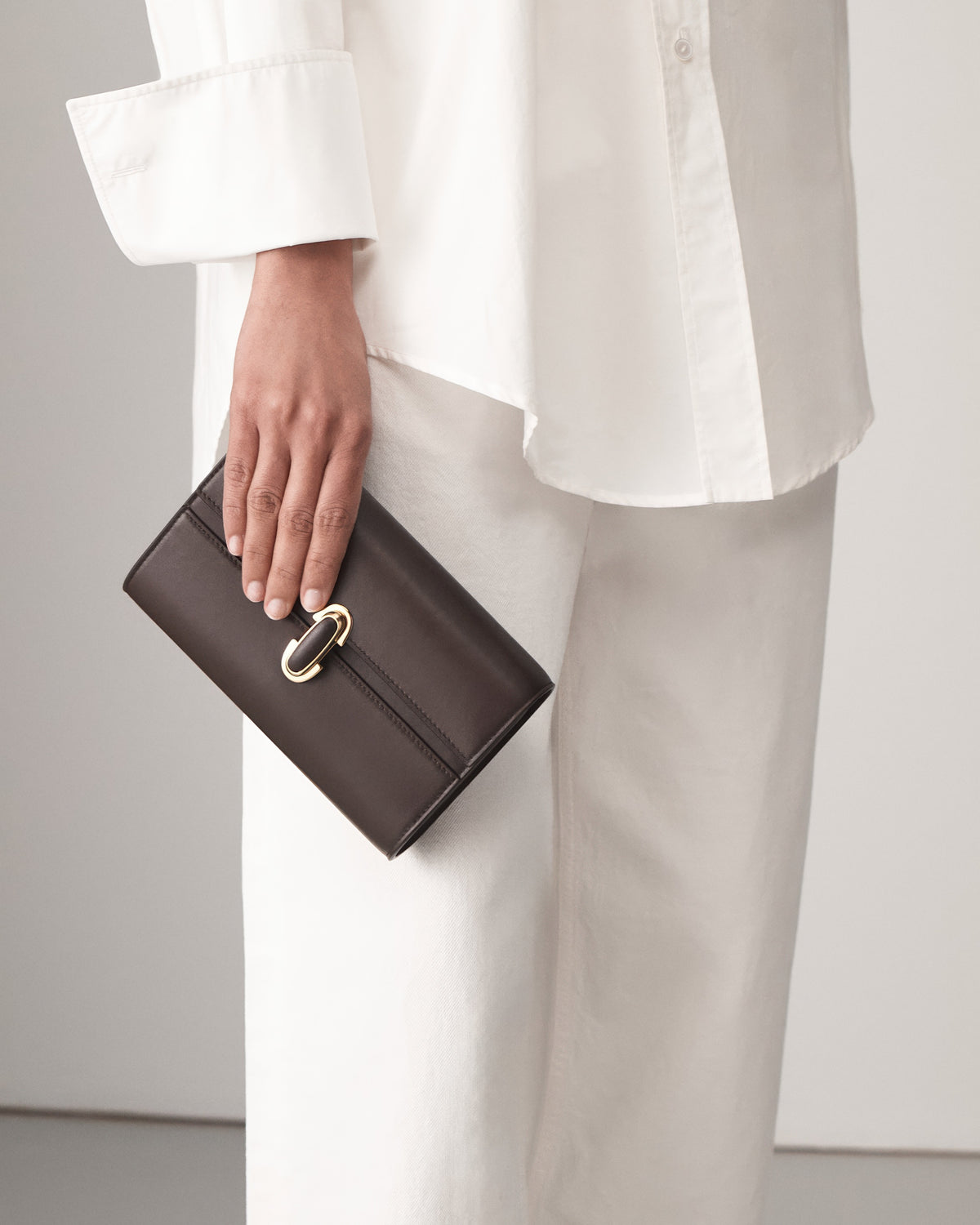 on model view of a coffee brown leather bag with a coffee brown leather covered gold clasp on a white background