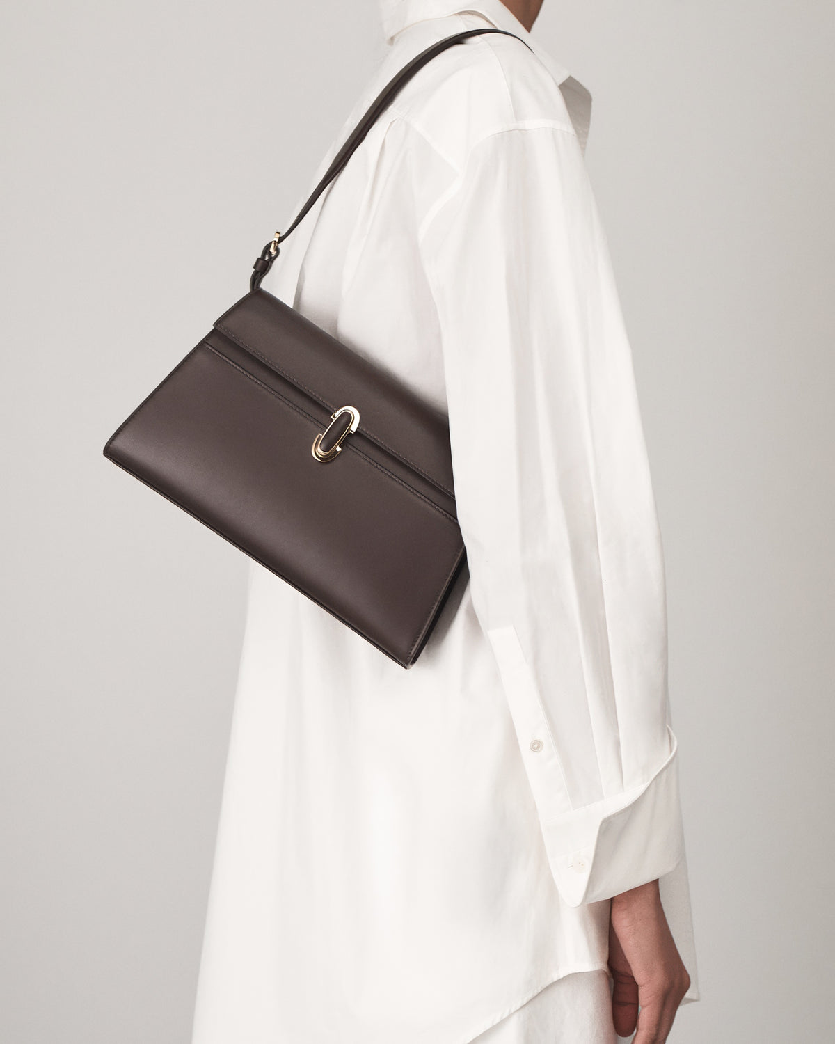 on-model view of a coffee brown leather shoulder bag with a leather covered gold clasp on a white background 