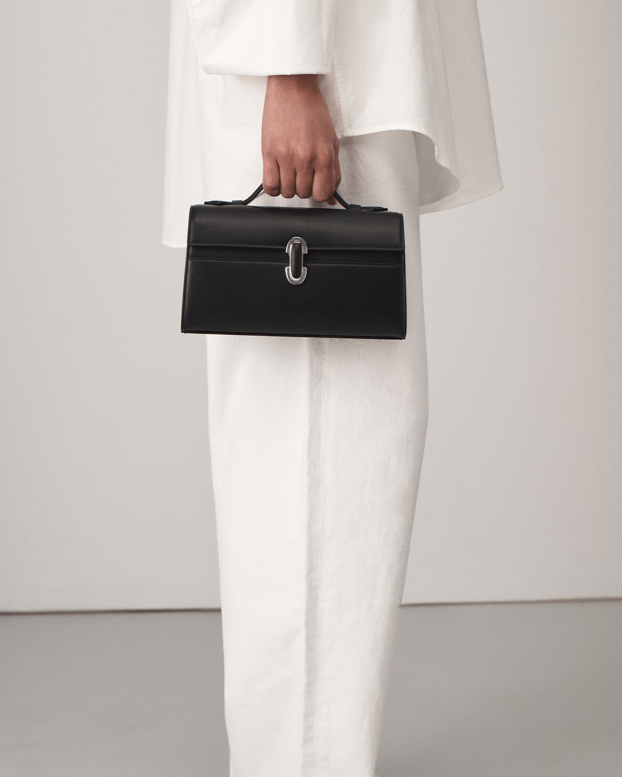 on model view of a black leather top handle bag with a black leather covered silver clasp on a white background