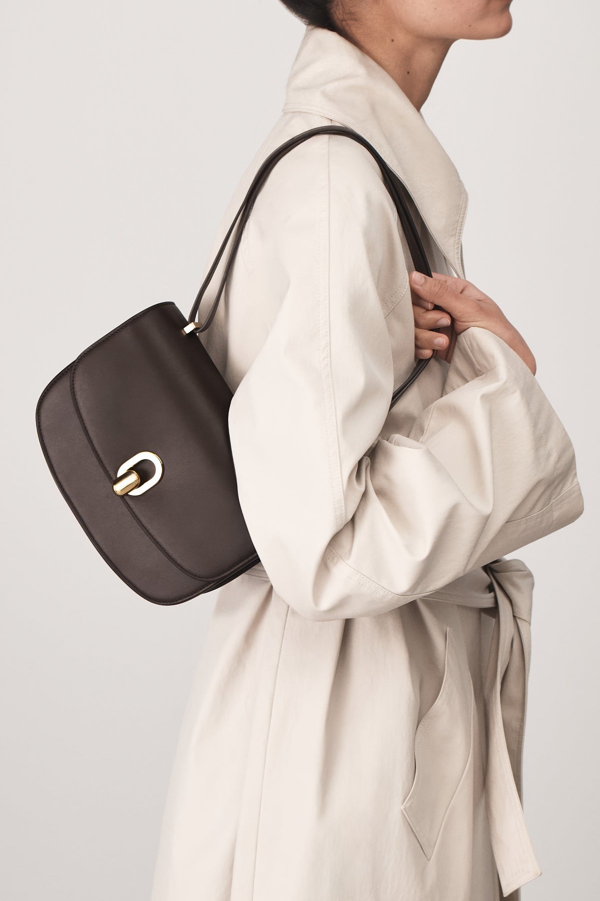 on model view of a coffee brown leather bag with gold hardware on a white background