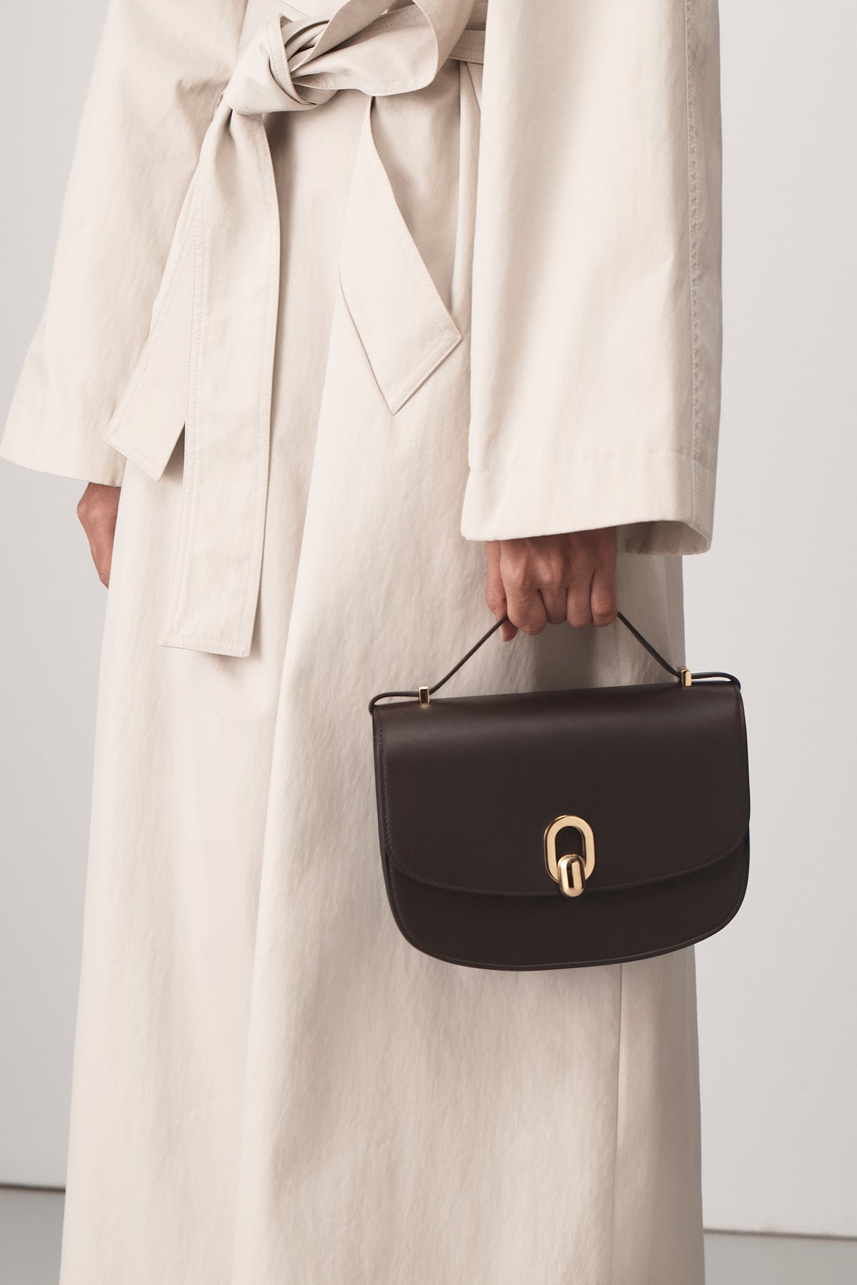 on model view of a coffee brown leather bag with gold hardware on a white background