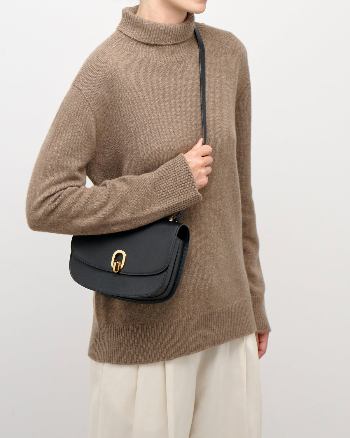 on model image of a black leather bag with gold hardware on a white background
