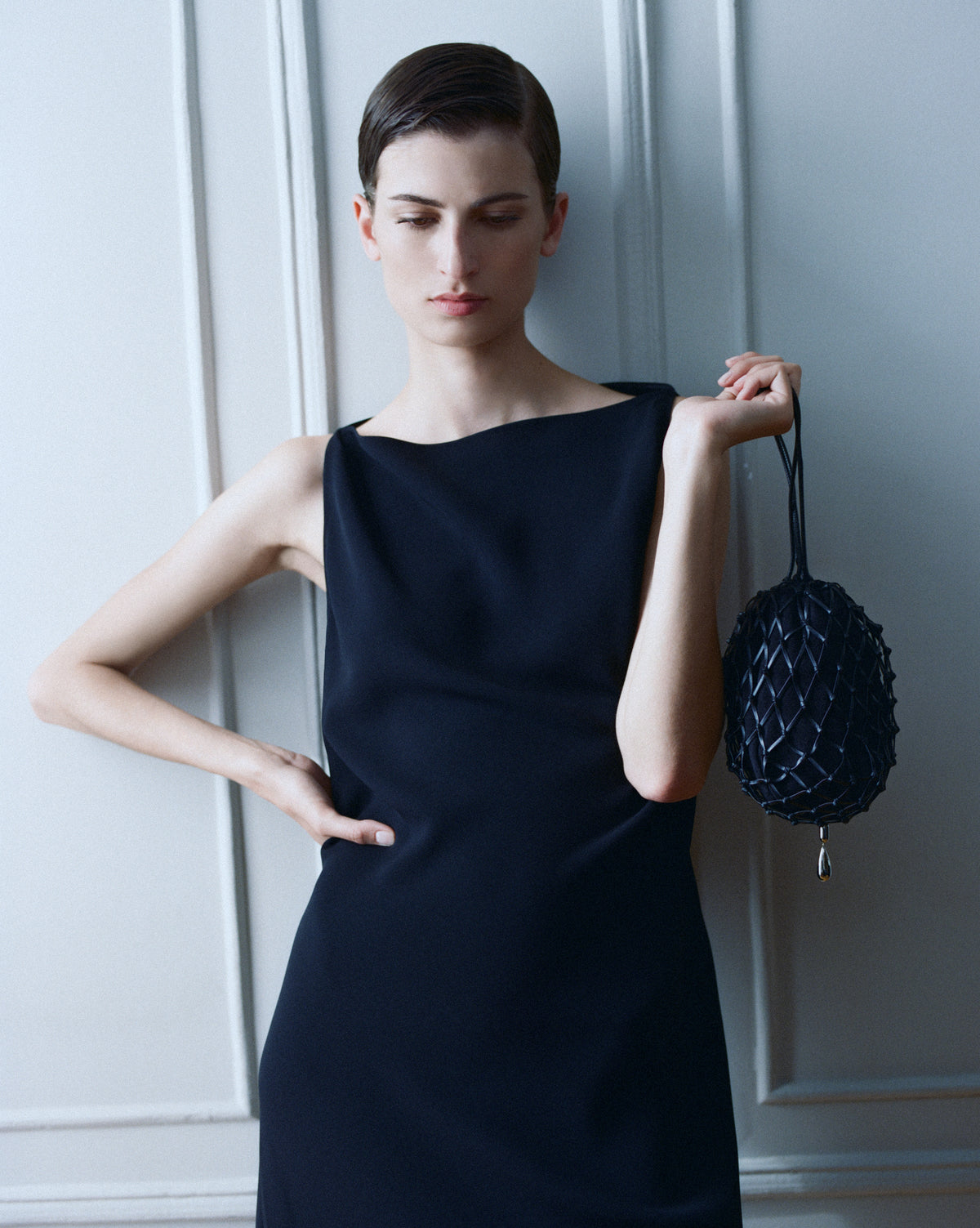 campaign on model image of a black macrame pouch with gold hardware against a white wall