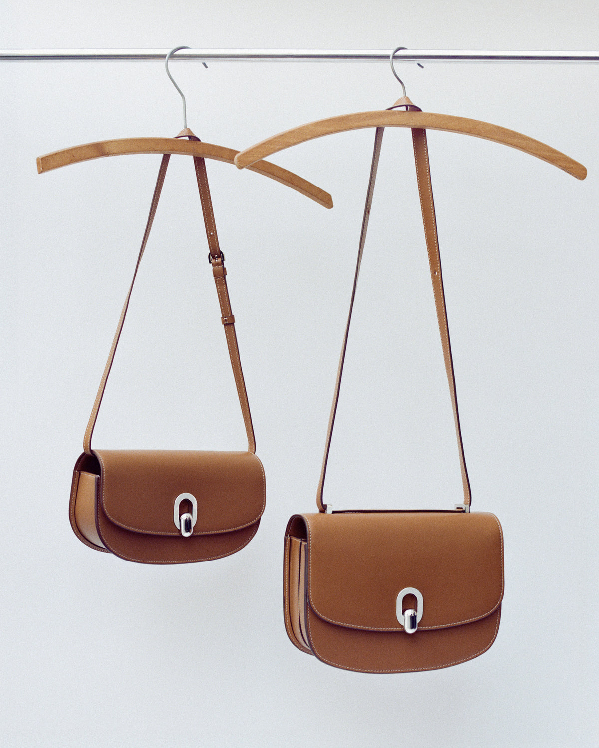 campaign image of two saddle brown leather bags with silver clasps on hangers on an off white background