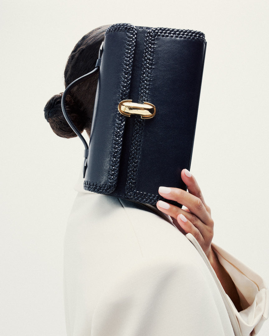 on model image of navy blue woven bag with gold clasp on a white background