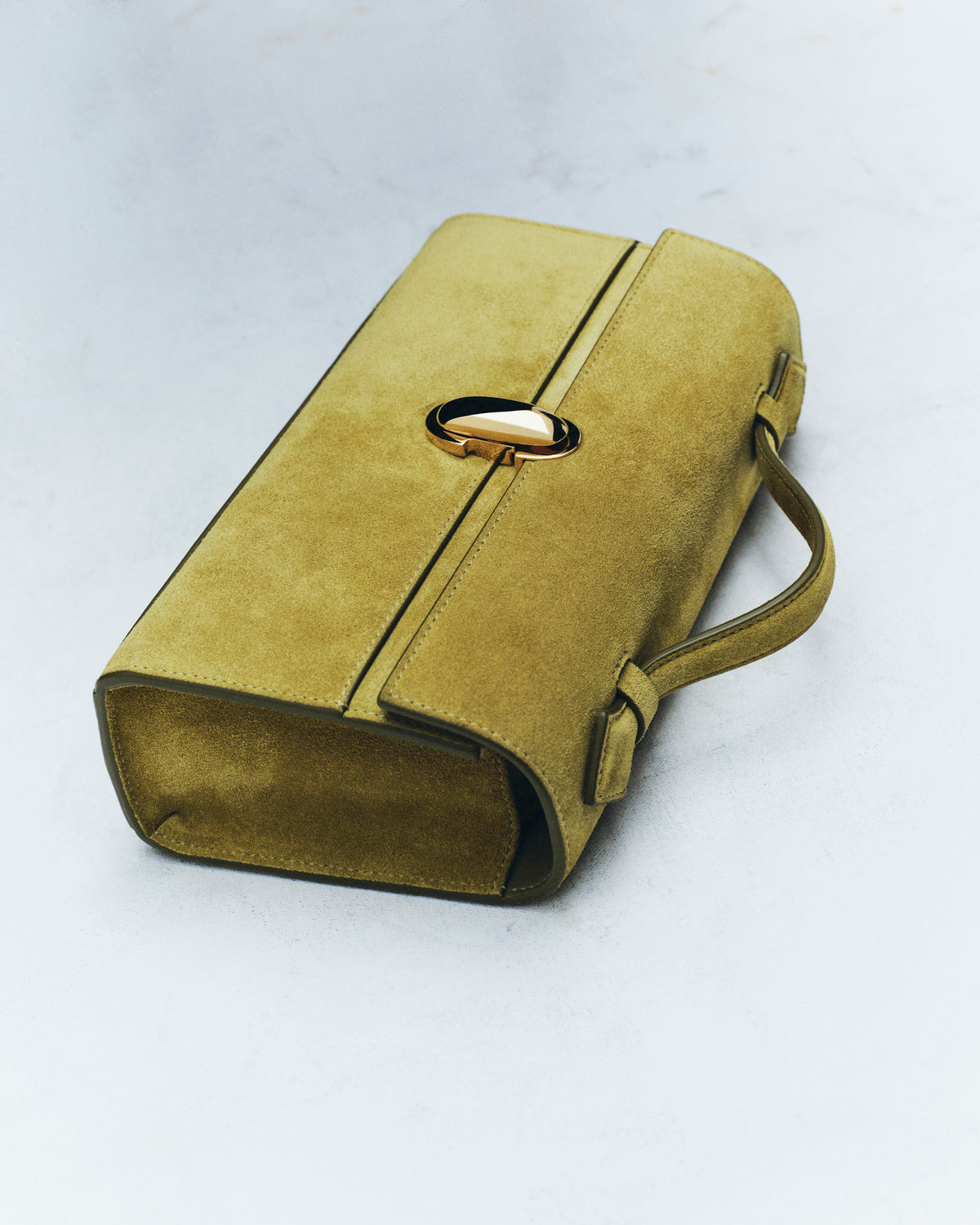 editorial image of a chartreuse green suede bag with a gold clasp on an off white background