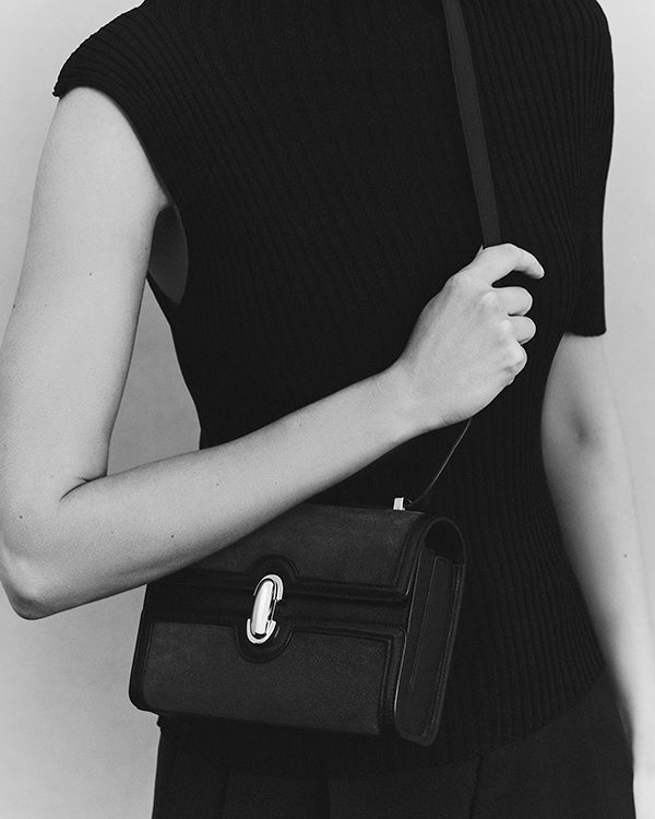 black and white editorial image of black bag on a grey background