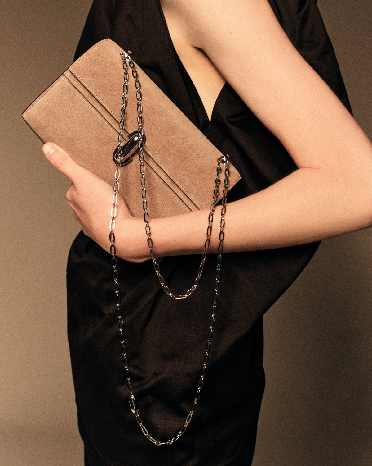 campaign on model image of a taupe brown suede bag with a silver clasp and silver chain on a brown background