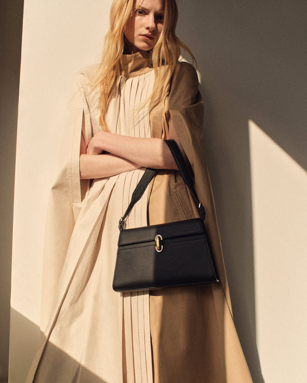 campaign on model image of a black leather bag with silver and gold clasp on a beige background
